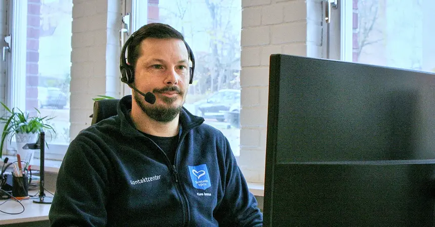 en person som har headset på sig och svarar i telefon framför en dator